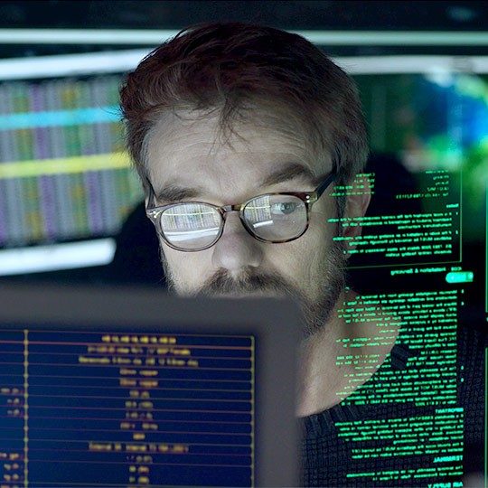 Man wearing glasses looking at various screens of comupter information