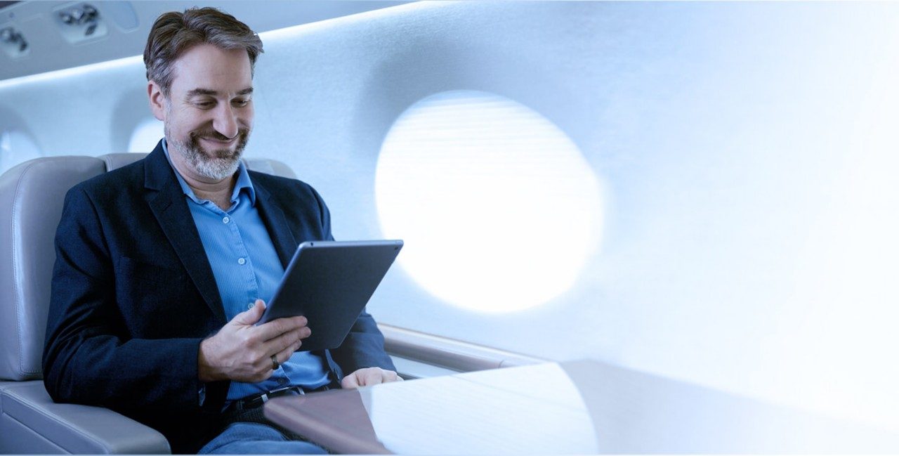 Man dressed in a suit jacket sitting in a private jet using airplane satellite internet to connect his tablet