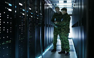 Two male warfighters utilizing defense technology looking at server racks