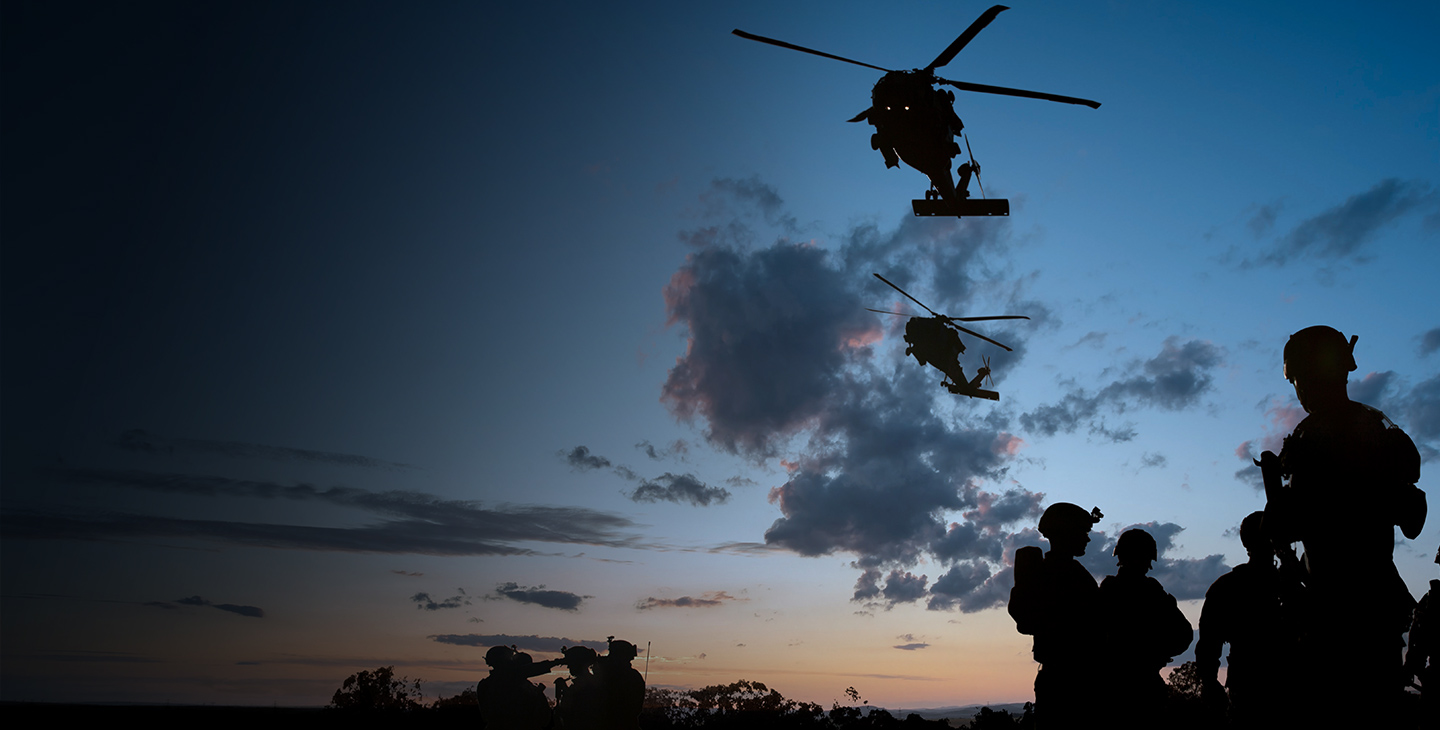 Rotary wing aircraft flying over soldiers utilizing defense technology at dusk 
