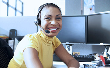 Female sales agent wearing a yellow shirt and headset, smiling at the camera